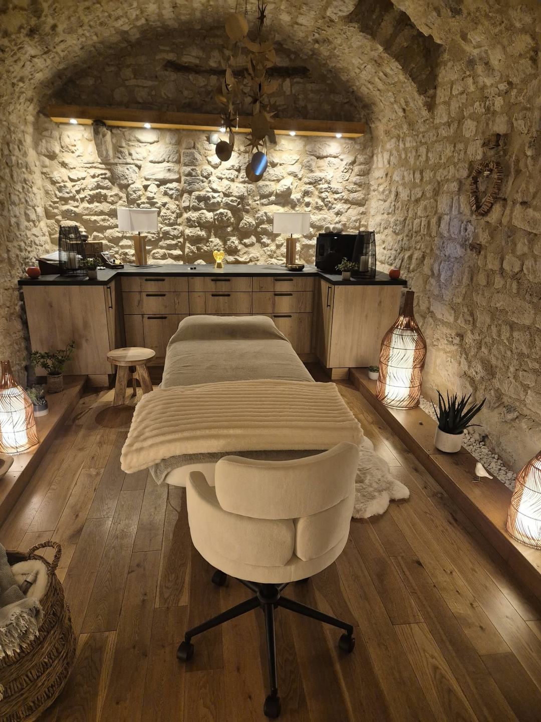 Salle de soin du cabinet de réflexologie : table de massage, murs en pierre voûtés, parquet en chêne et lampes tressées à la lumière douce